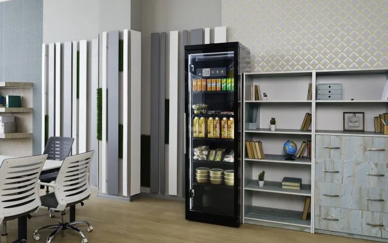 Black cabinet with a glass door in an office with desks and chairs, juice, snacks and cups on the shelves