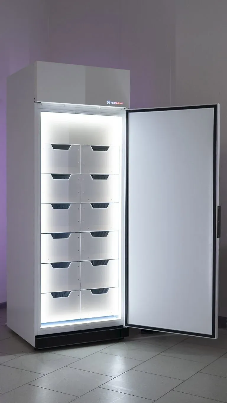 White cabinet with its solid door open, six tiers of empty white trays inside